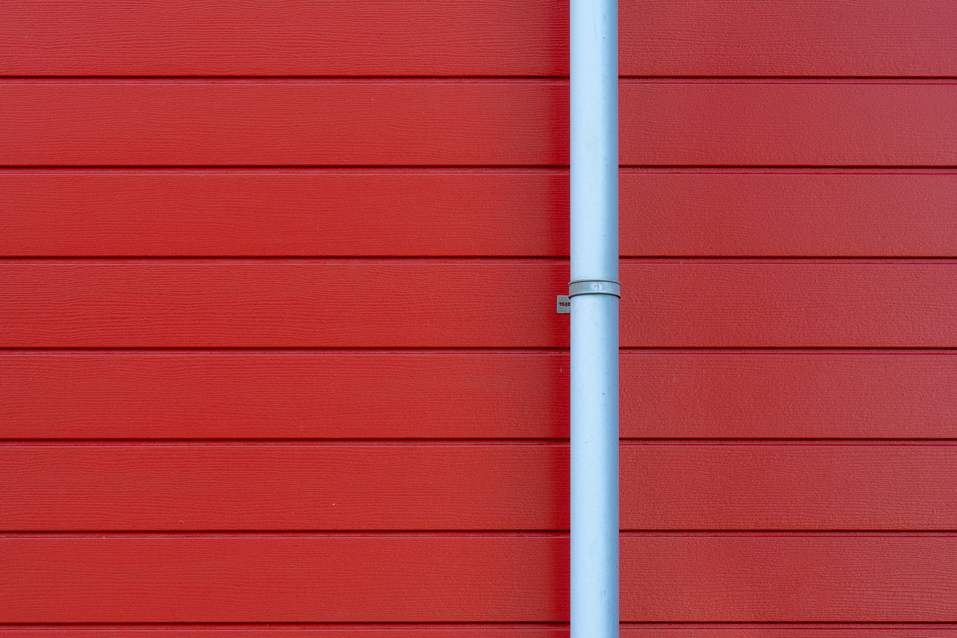 A minimalist photo of a red wall with a white rain gutter, showing clean lines and vibrant color contrast.