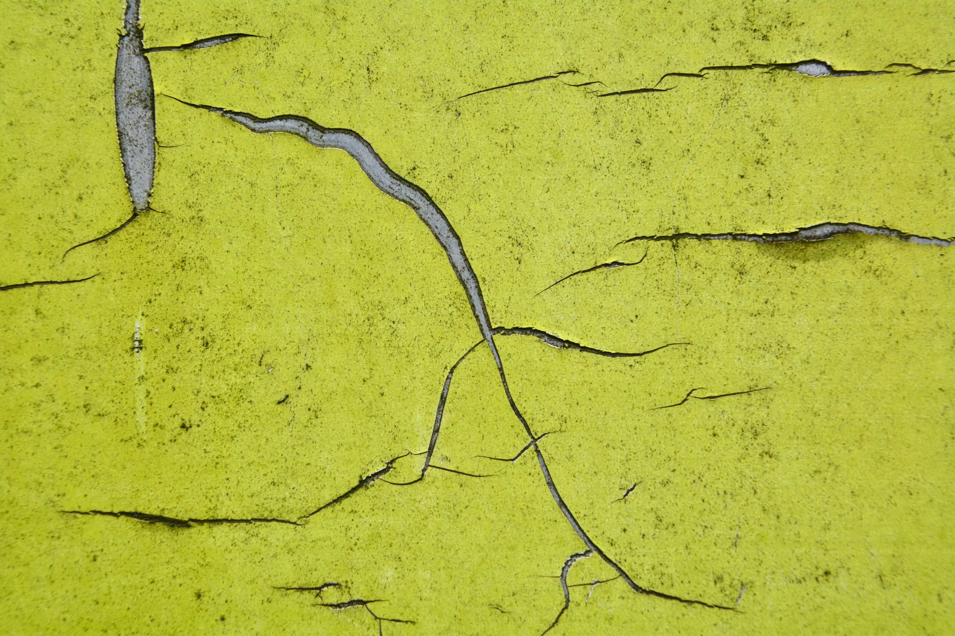Detailed close-up of a cracked yellow painted wall, showcasing texture and patterns.