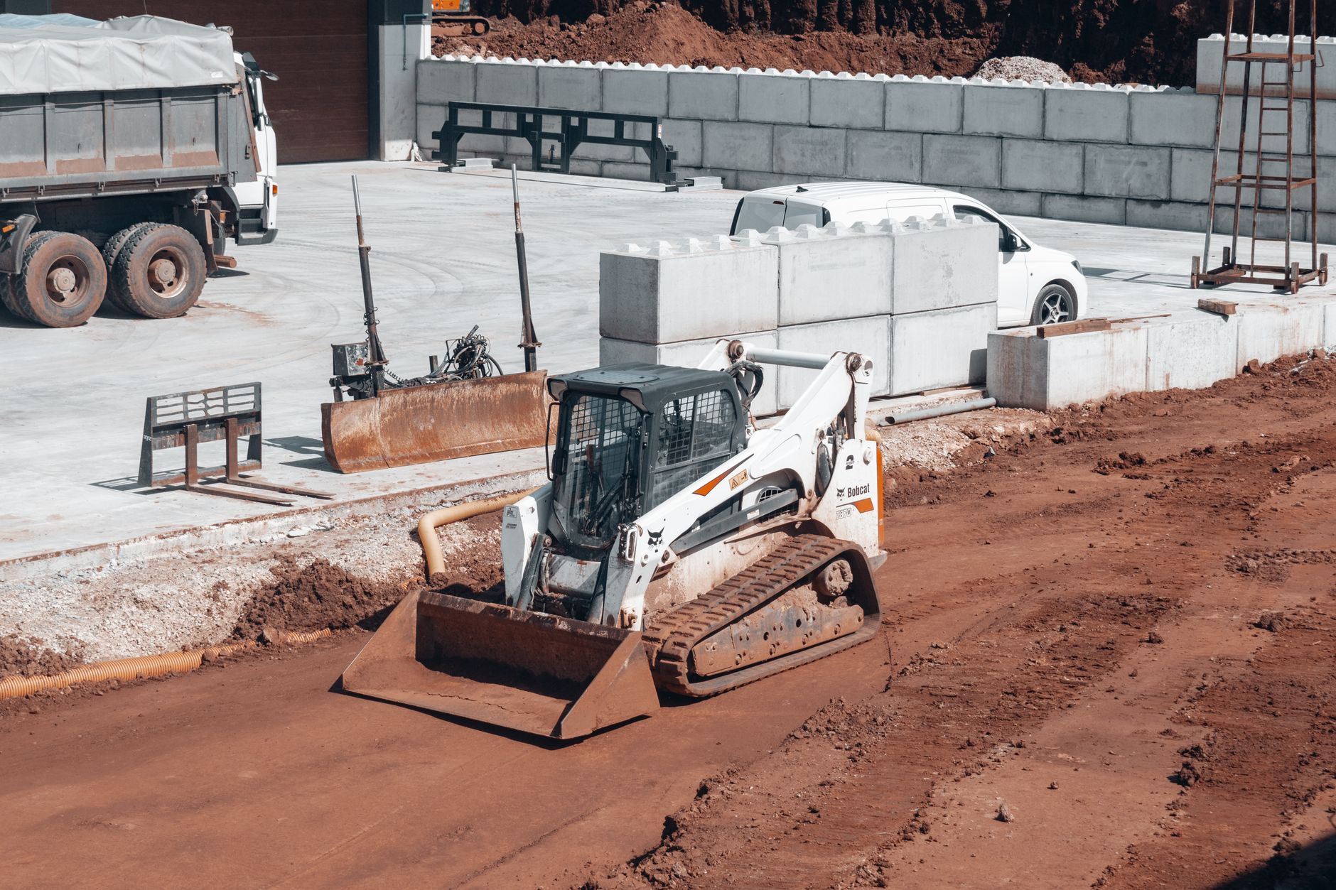 Bulldozer working on a construction site alongside a white truck and concrete blocks.