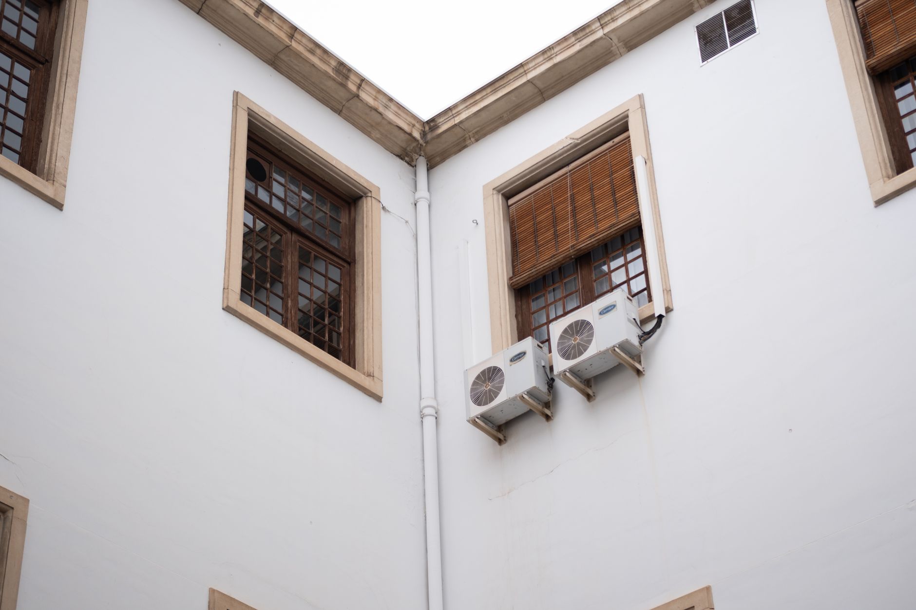 White building facade with wooden window shades and air conditioning units.