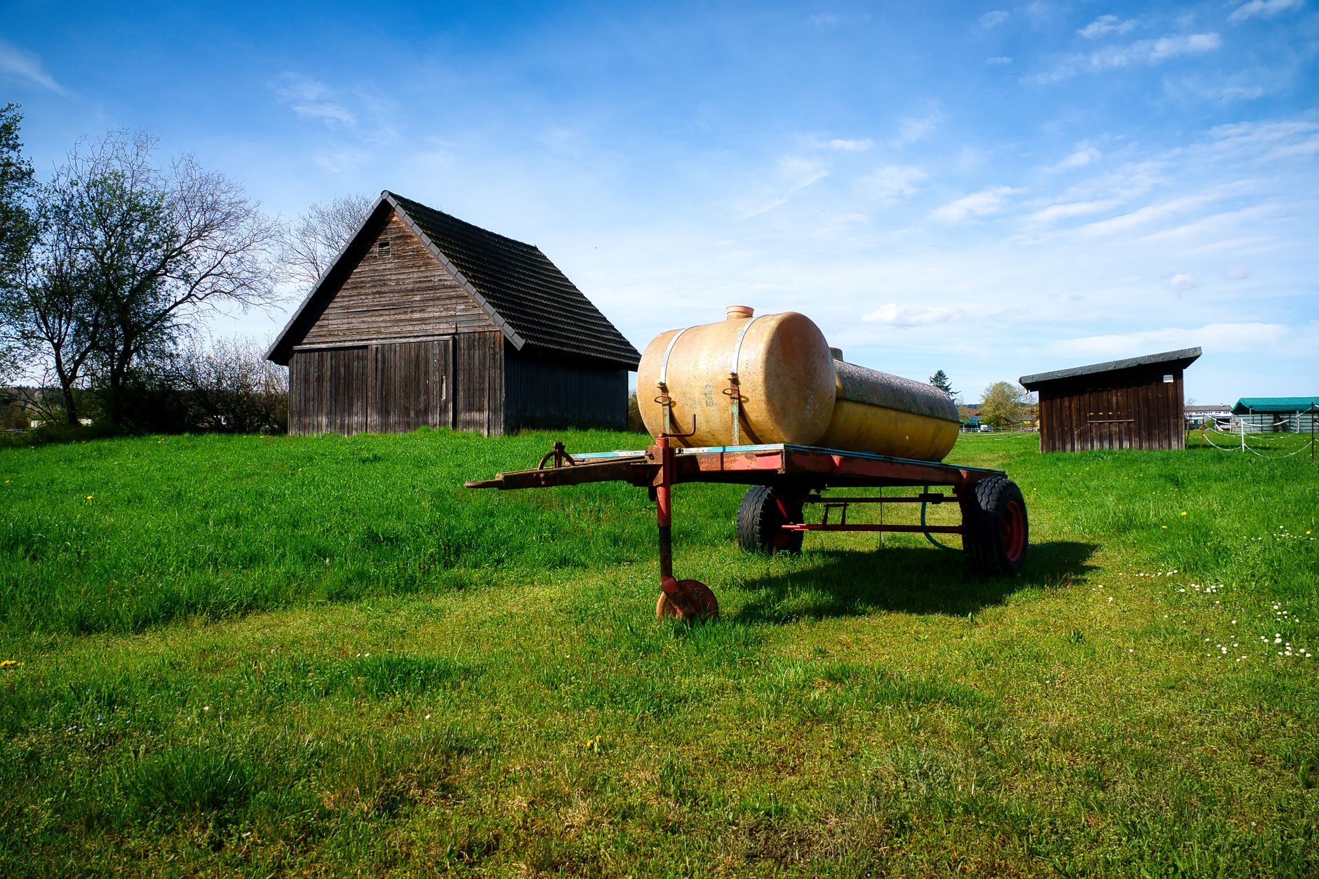 A rustic water tanker sits on a lush green field in Pforzheim, Germany, against a bright blue sky.