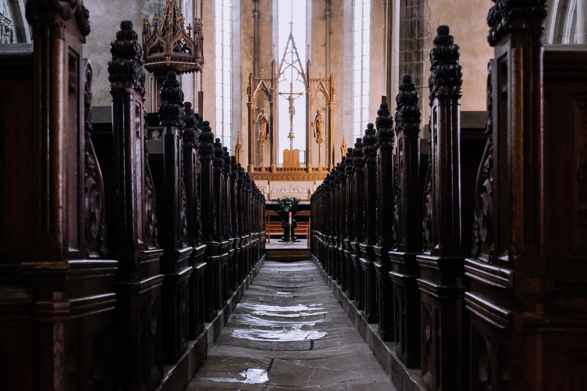 Explore the intricate architecture of a Gothic church interior focusing on the altar and wooden pews.