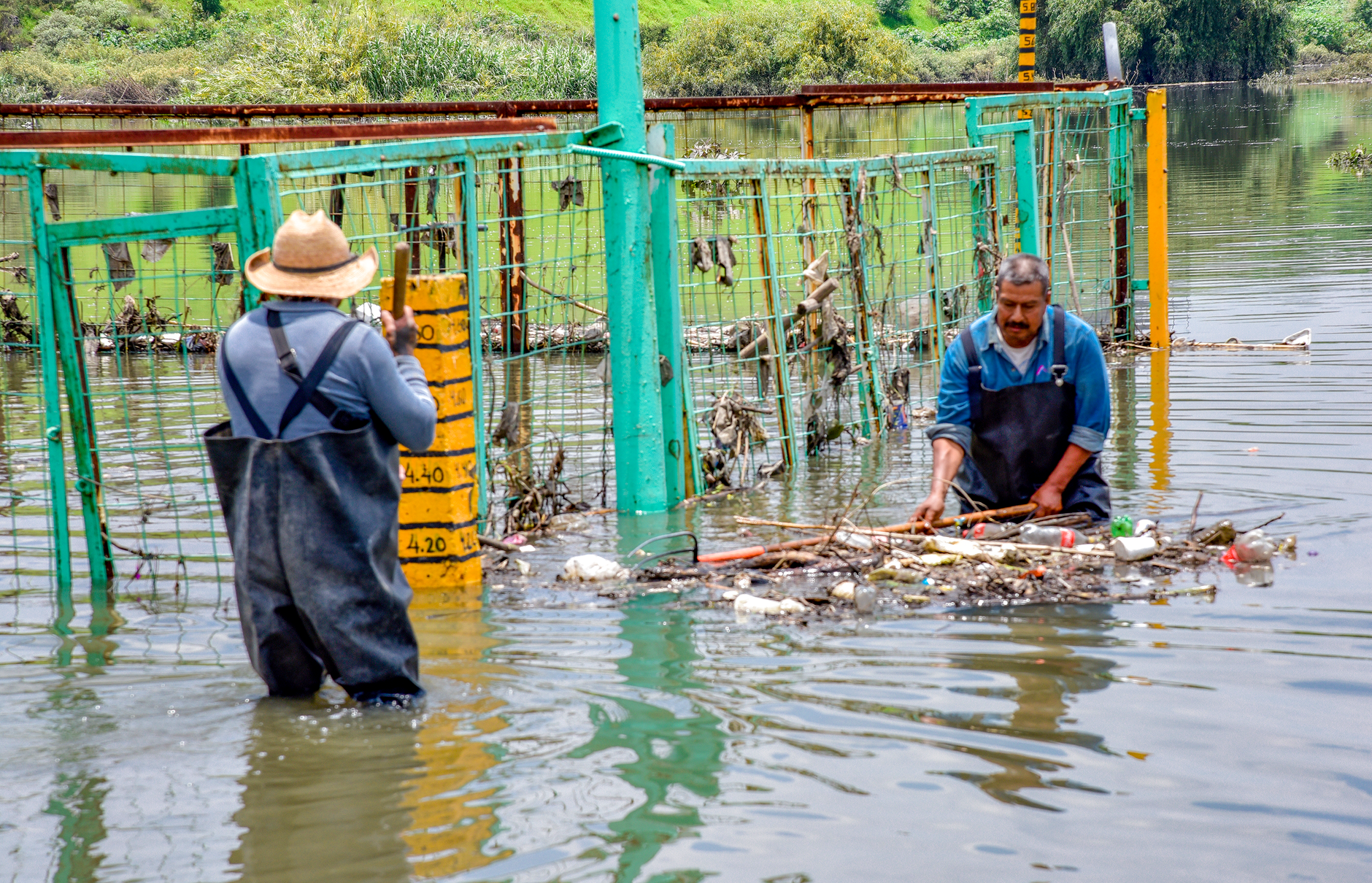Two men working to clear trash from a flooded area, focusing on water pollution and urban flooding.