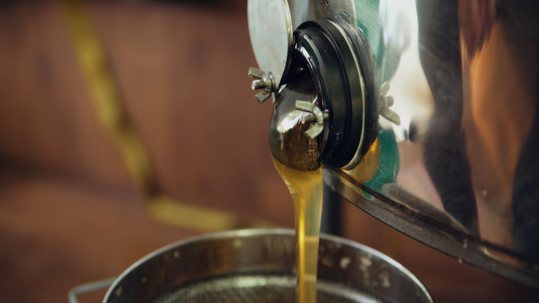 Close-up of honey pouring from an extractor spout into a strainer, highlighting honey production.