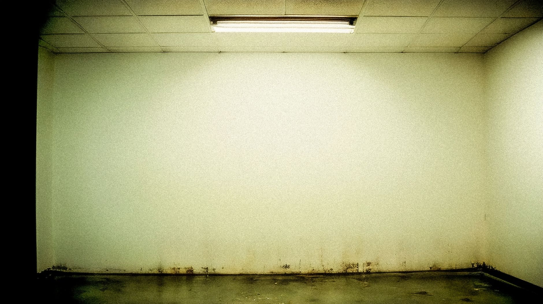 Moody grunge-style room with stained walls and fluorescent ceiling light.