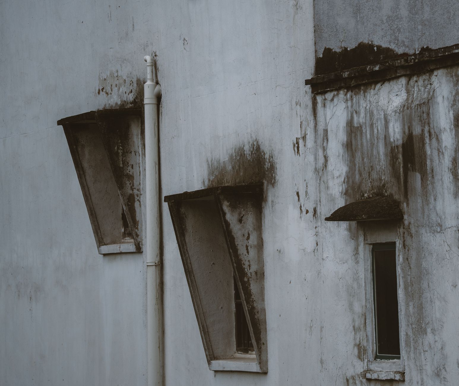 Close-up of a weathered building facade featuring rustic, tilted windows and peeling paint.