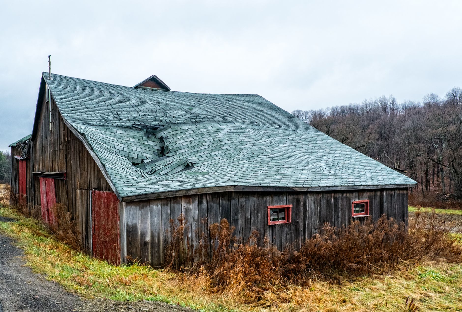 A weathered wooden barn with a damaged roof in a rural New York landscape.