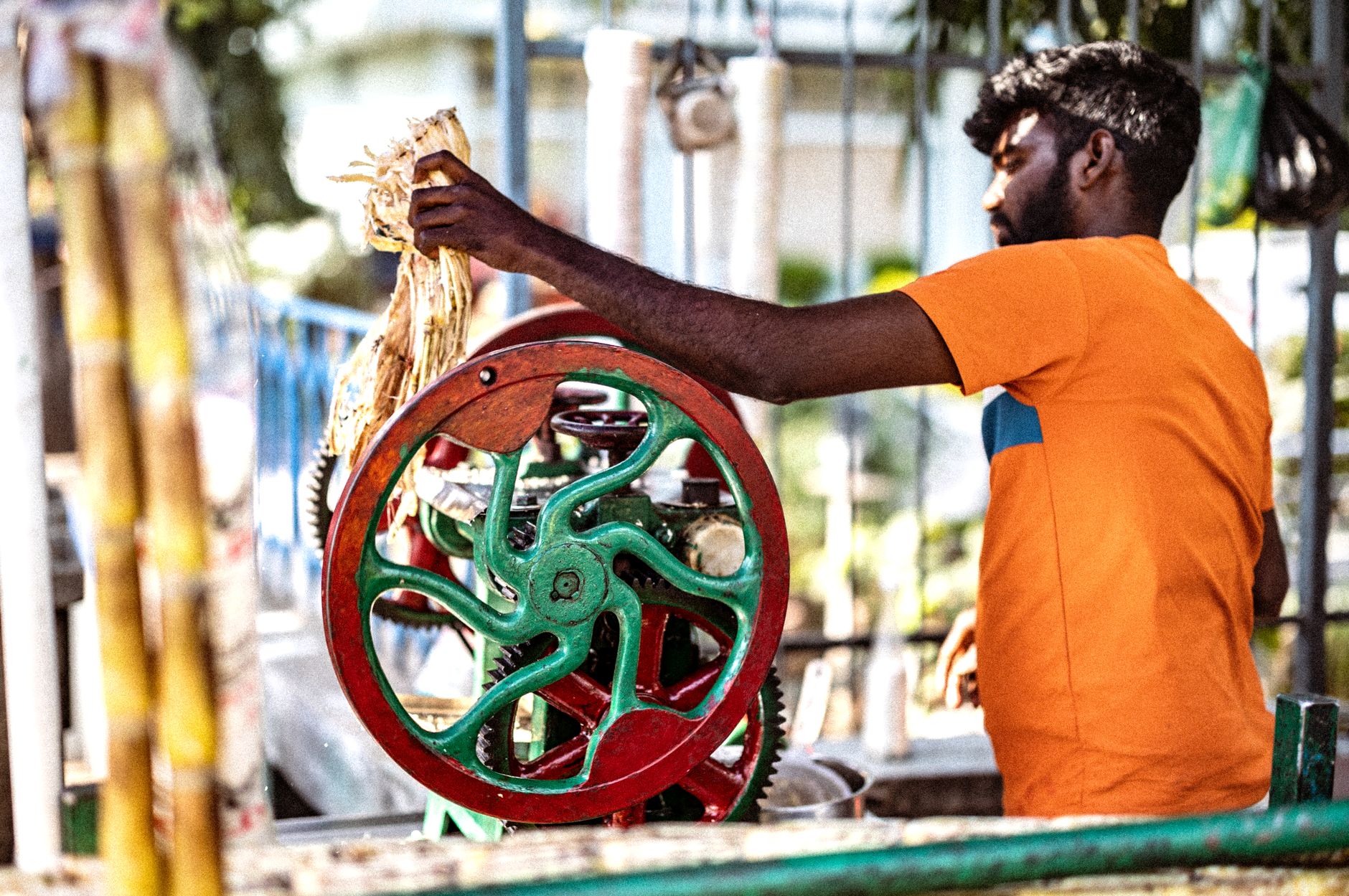 South Asian man using a traditional machine for extracting fresh sugar cane juice on a sunny day.